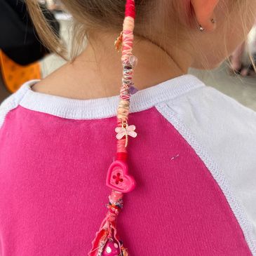 Colorful braided hair accessory with beads and charms on a child's ponytail.