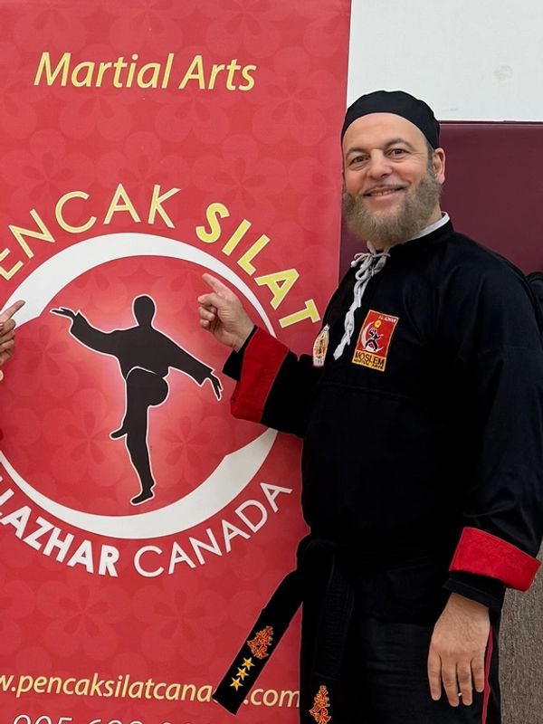 Man in martial arts uniform pointing at Pencak Silat sign.