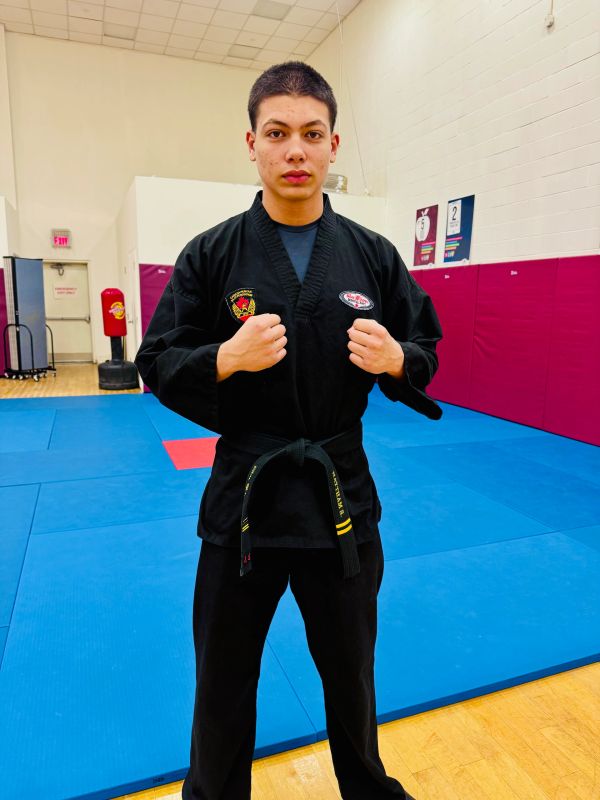 Young martial artist in black uniform with black belt on training mat.