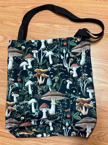 Tote bag with mushroom and plant pattern on wooden floor.