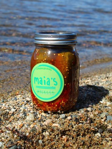 Jar of Maia's pickles on a rocky shore by the water.