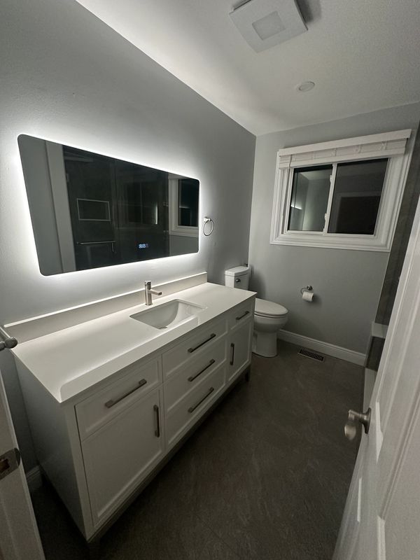 Modern bathroom with illuminated mirror and sleek white vanity.