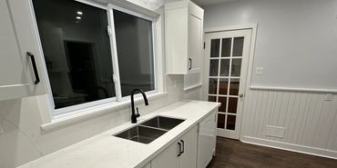Modern white kitchen with marble countertops and dark wood flooring.
