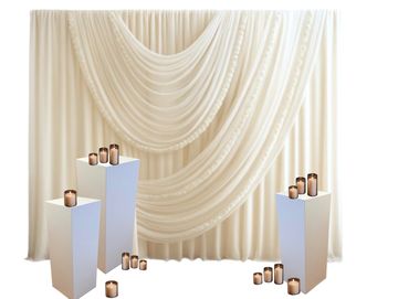 Elegant cream backdrop with draped fabric and candles on white pedestals.