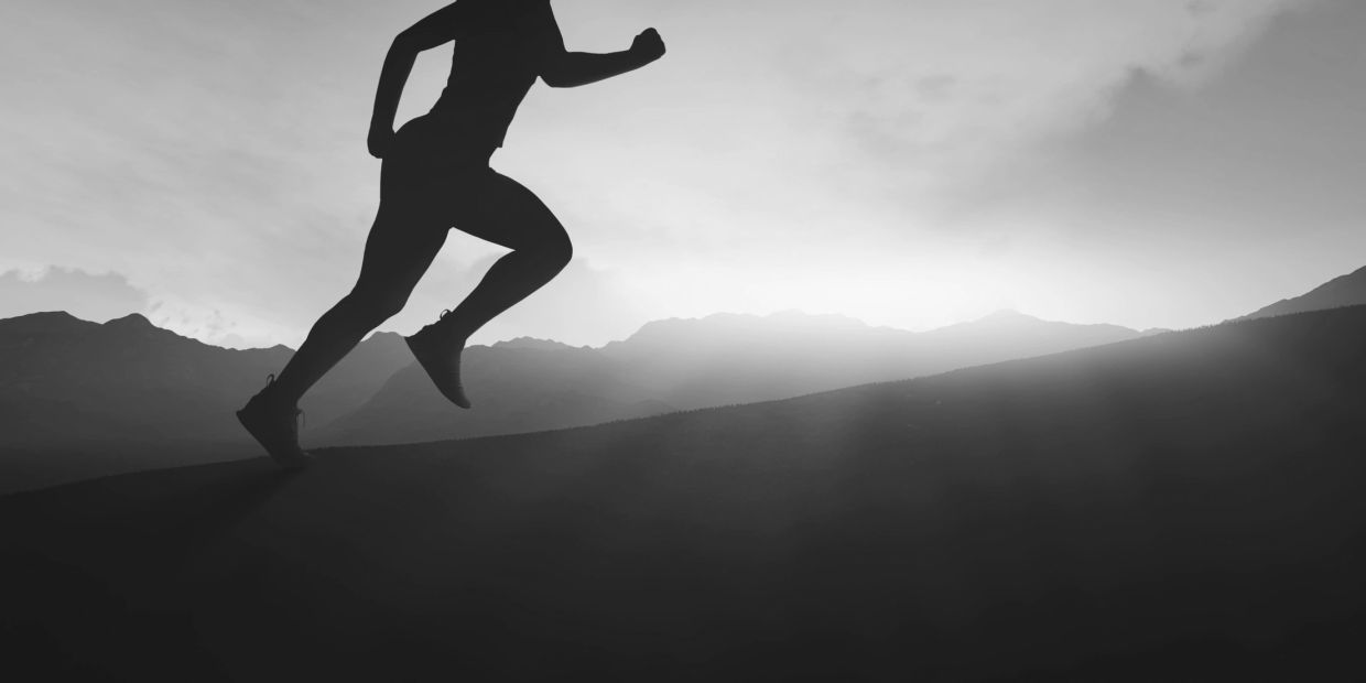 Silhouette of a person running uphill against a mountainous sunrise.