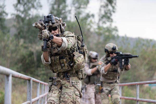 Three individuals in camouflage military gear holding rifles in an outdoor setting.