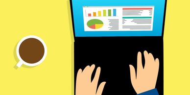 Hands working on a laptop with charts and coffee nearby.