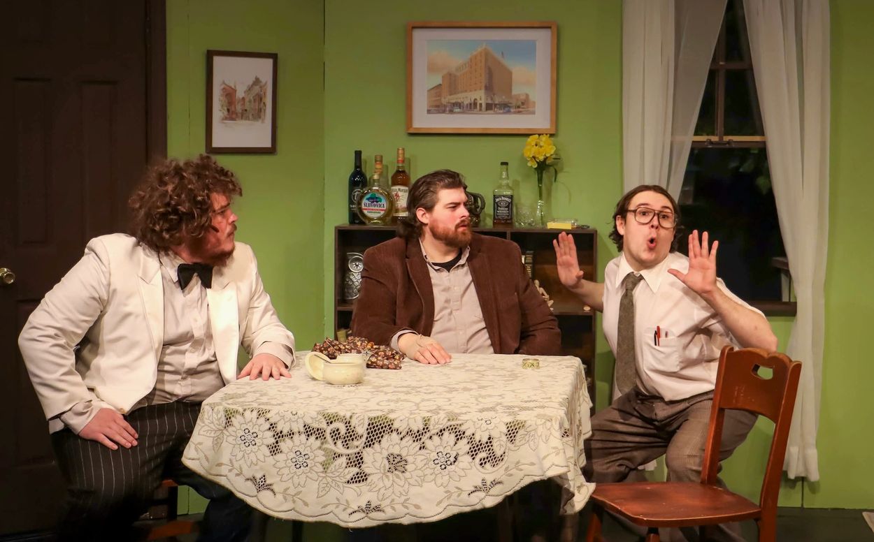 Three men in vintage attire sitting around a table in a retro-styled room.