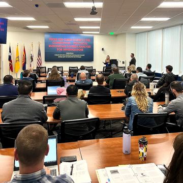Classroom seminar with attendees listening to presenters in front.