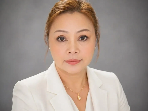 Professional woman in white blazer with gold necklace against gray background.