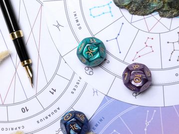 Astrological chart with zodiac-themed dice and a fountain pen.