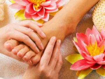 Hands giving a relaxing foot massage surrounded by pink flowers.
