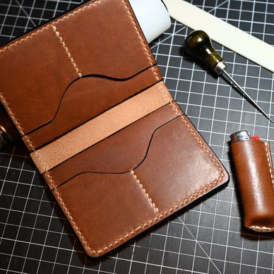 Handcrafted brown leather wallet with tools on a cutting mat.