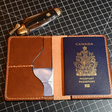 A Canadian passport in a brown leather holder on a black grid mat with a pocket knife.