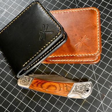 Two leather wallets and an ornate folding knife on a grid mat.