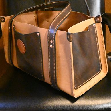 Handcrafted leather tote bag resting on a black leather and wood chair.