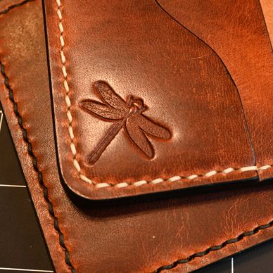 Close-up of a brown leather wallet with a dragonfly embossing.