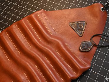 Handcrafted brown leather tool roll with stitched compartments and embossed leather tags.