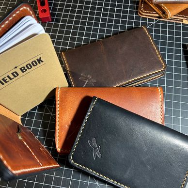 Handcrafted leather wallets and a field book on a cutting mat.