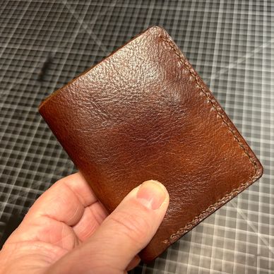 Hand holding a brown leather wallet with visible stitching.