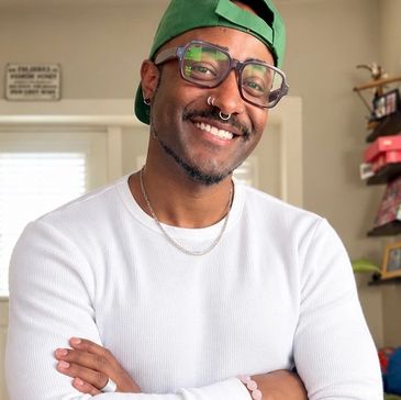 Smiling man in glasses and green cap indoors.