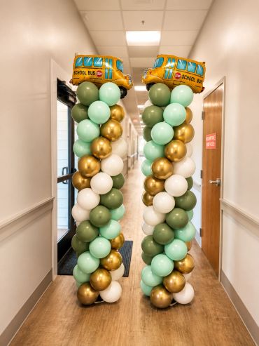 Balloon columns with school bus toppers in a hallway.