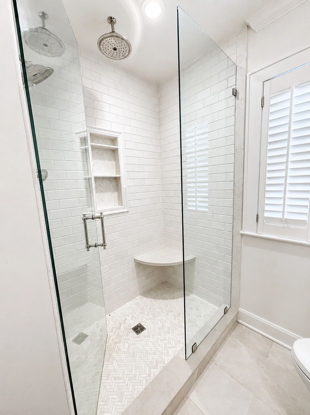 Bright, modern glass shower with white subway tiles and built-in bench.