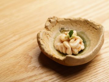 Small artistic dish with creamy garnish on wooden surface.