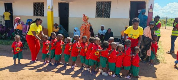 Children lined up outside a school building with caregivers.