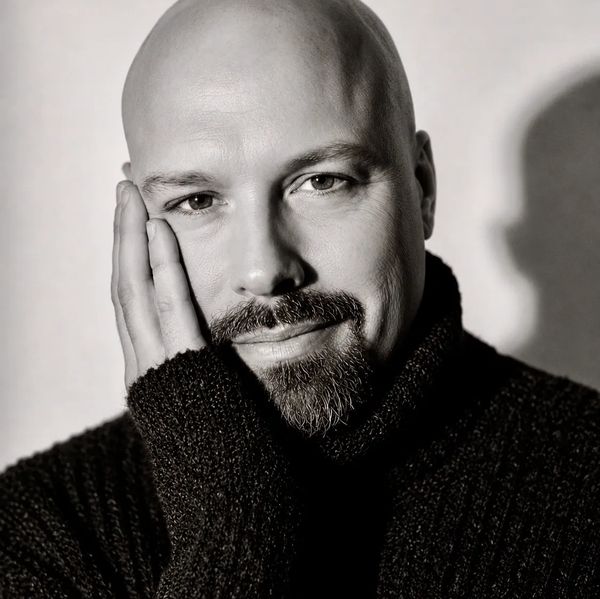 Portrait of a bald man with a beard resting his face on his hand.
