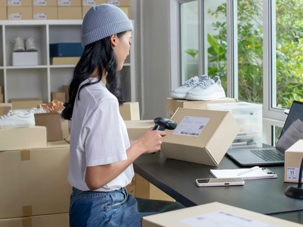 Woman scanning a package in a home office surrounded by boxes and shoes.
