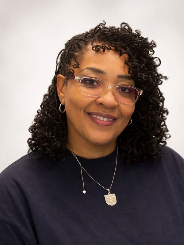Woman with curly hair and glasses smiling.