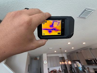 Hand holding thermal camera showing heat patterns on a ceiling indoors.