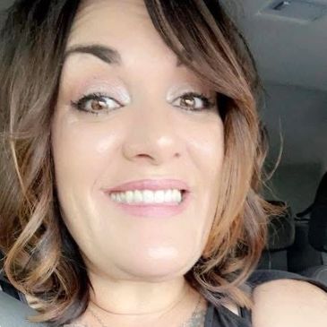 Woman smiling inside a car with light makeup and styled hair.