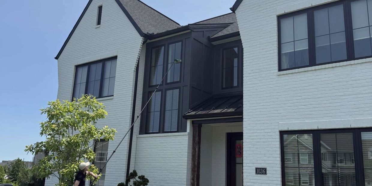 Technician using pure water pole system on a luxury white brick home exterior