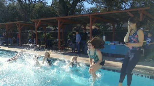 Kids jumping into a swimming pool on a sunny day.