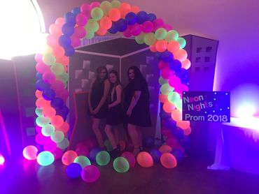 Three girls posing under a colorful balloon arch at Neon Nights Prom 2018.