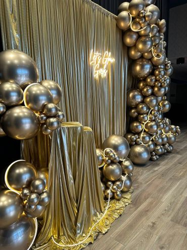 Elegant gold-themed event setup with balloons and draped fabric.
