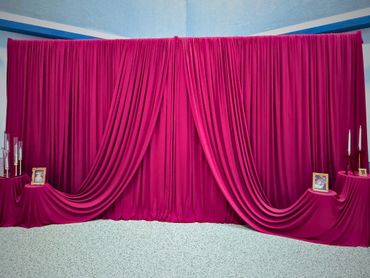 Elegant magenta draped curtain backdrop with framed photos and candles.