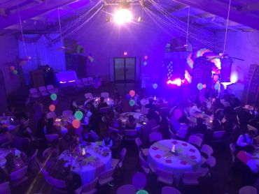 People gathered at a dimly lit party with purple lighting and balloons.