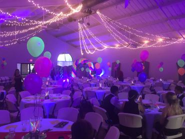 Decorated party hall with balloons and string lights.