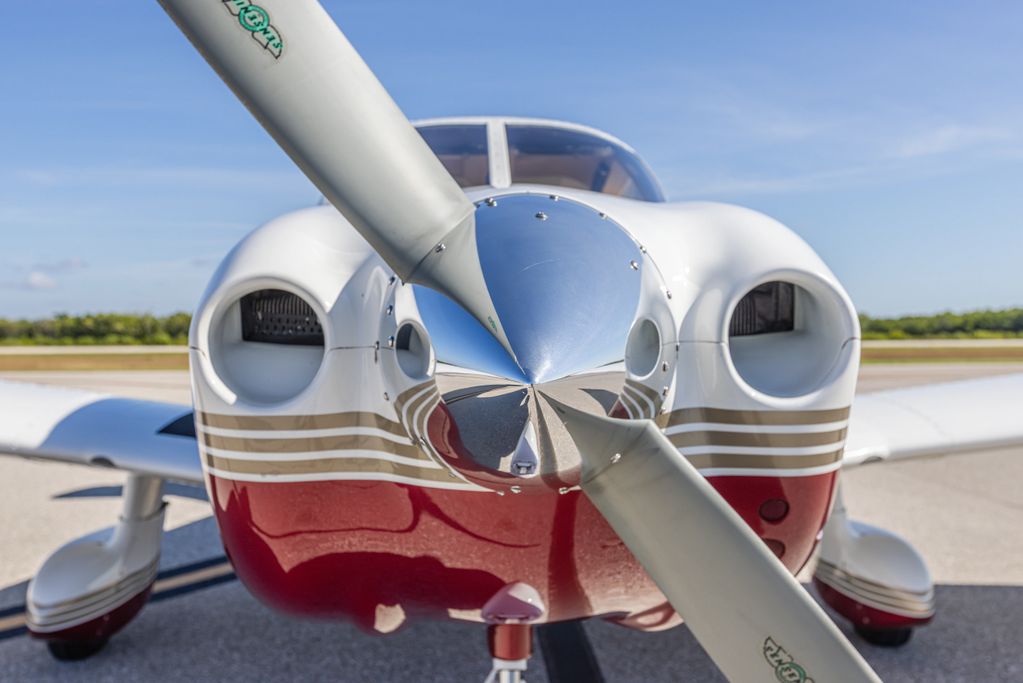Close-up of a propeller airplane's nose and propeller blades on a sunny day.