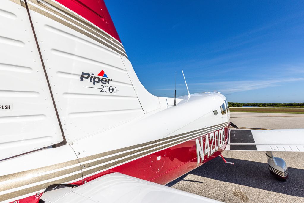 Close-up of a Piper 2000 airplane tail section on runway under clear blue sky.