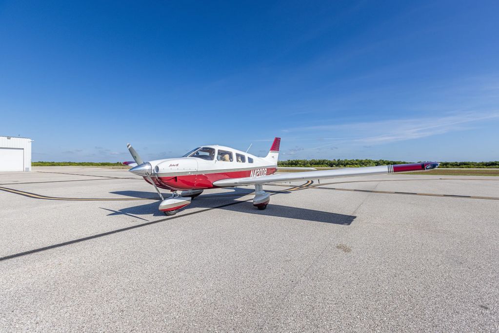 Small red and white single-engine airplane on runway under clear blue sky.