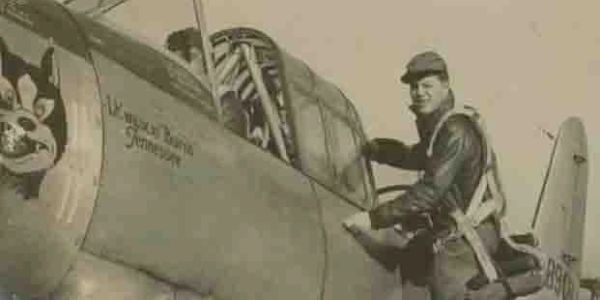 Pilot standing next to vintage military airplane.