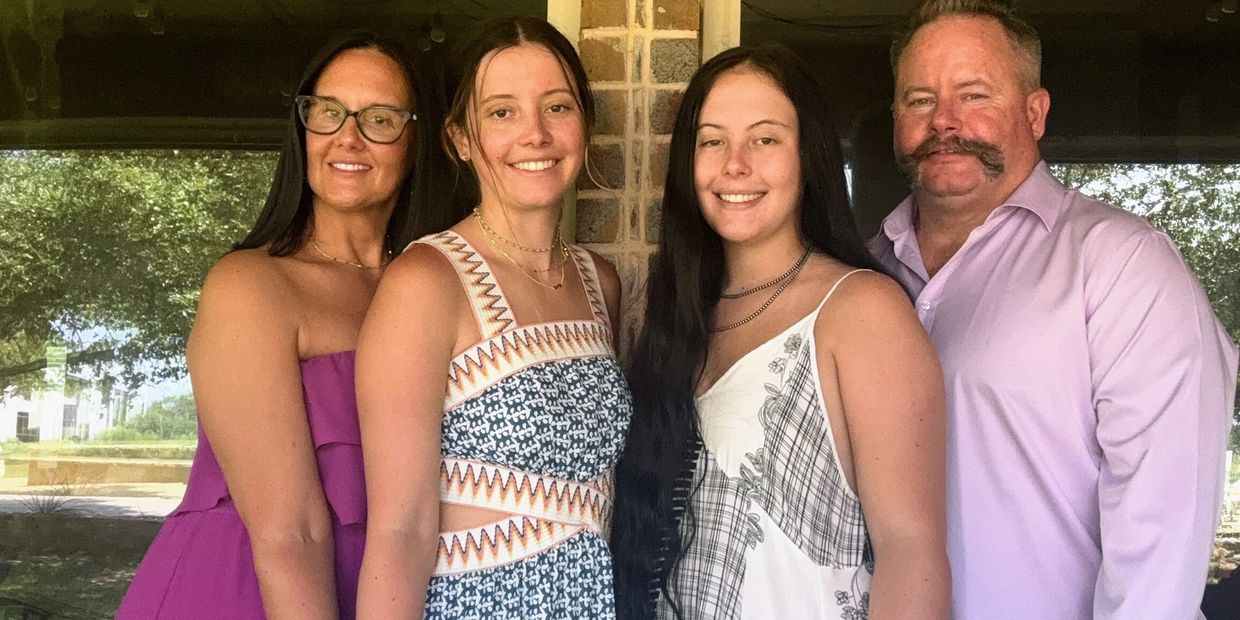 Family portrait with three women and one man standing in front of a brick wall.