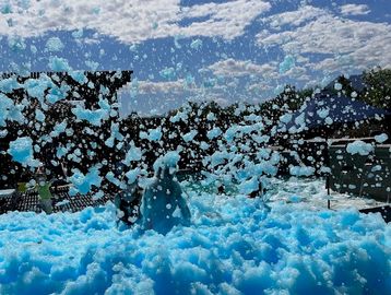 People playing in blue foam outdoors under a partly cloudy sky.