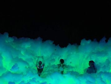 Three people in glowing foam at night.