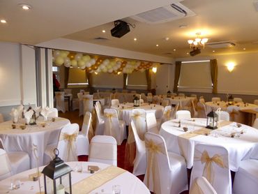 Gold sashes on white chair covers and gold cream and white balloon Garland 