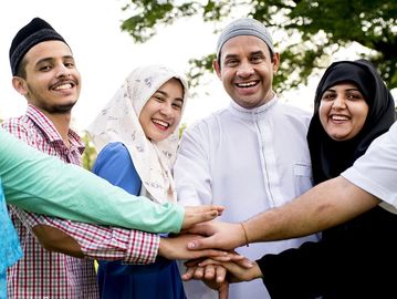 Group of Muslim friends smiling and joining hands in unity outdoors.
